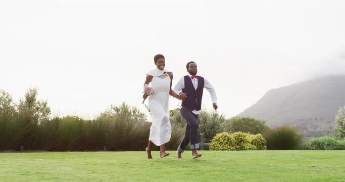Happy african american couple holding hands and jumping during wedding