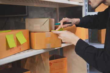 Shipping shopping online, startup small business owner writing address on cardboard box at workplace. Freelance Asian man small business entrepreneur SME working with box at home. Focus at box.