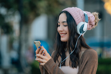 girl in winter with hat on the street with mobile phone and headphones