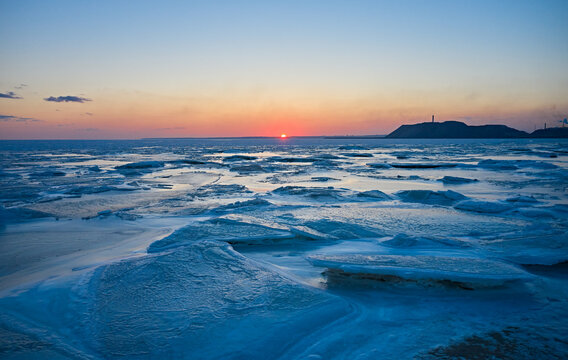 Aerial view of sunset over the frozen sea. Winter landscape on seashore during dusk. View from above of melting ice in ocean on sunrise with horizon. Global warming. Vivid colorful skyline scenics.