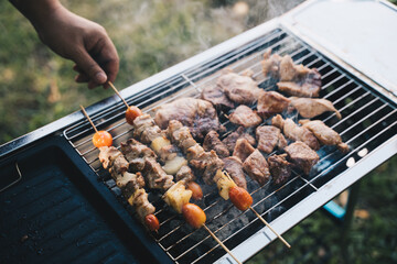 Hand of young man grilling some meat and vegetable-meat skewers on huge gas grill.
