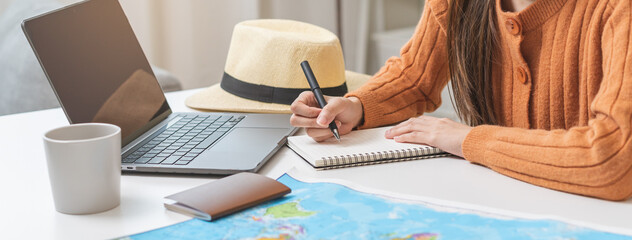 Travel planning, vacation, holiday trip concept, asian young tourist woman hand take note, check list using laptop searching information booking ticket or hotel online, preparation for journey trip. - obrazy, fototapety, plakaty