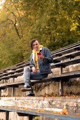 Fototapeta premium Young man with dreadlocks browsing mobile phone, sitting on old shabby bench of street bleacher.