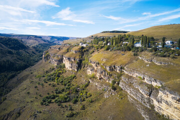 A mountain gorge with rocky slopes and a mountain village in the greenery above. Shooting from a drone.