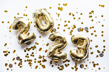 Carelessly scattered balloons made of gold foil in the form of the numbers 2023 with confetti on a...