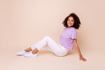 Photo of good mood gorgeous girl perming coiffure dressed striped t-shirt sitting relaxing on vacation isolated on beige color background