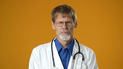 Portrait of tired handsome doctor man in professional medical white coat is isolated on yellow...