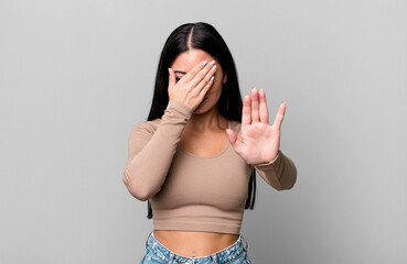 pretty latin woman covering face with hand and putting other hand up front to stop camera, refusing...