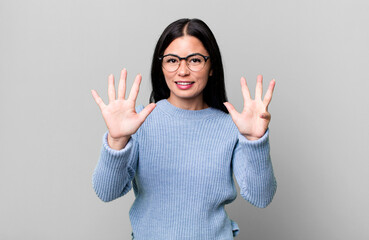 pretty latin woman smiling and looking friendly, showing number nine or ninth with hand forward,...