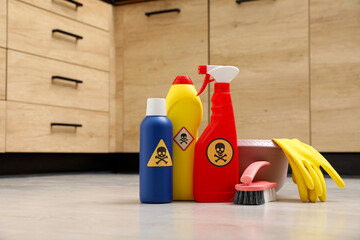 Bottles of toxic household chemicals with warning signs, gloves and brush on floor indoors, space...
