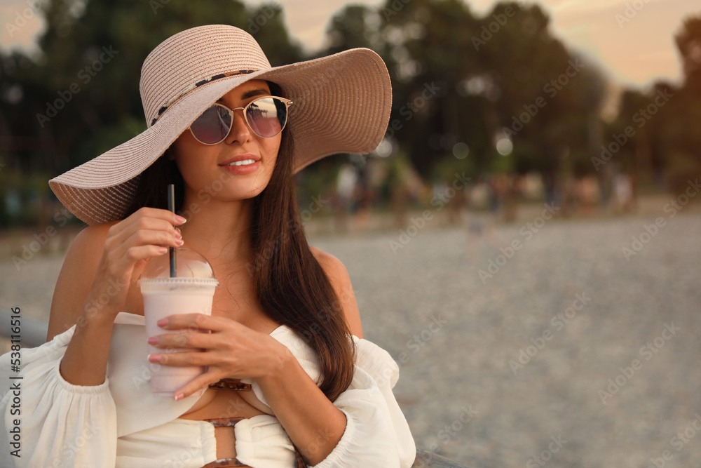 Wall mural Beautiful young woman with tasty milk shake outdoors, space for text