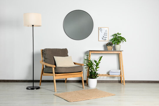 Stylish living room interior with wooden furniture, houseplants and round mirror on white wall