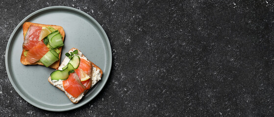 Tasty toasts with salmon, cream cheese and cucumber on dark table, top view with space for text....