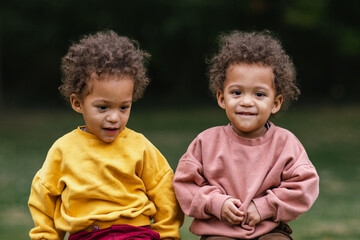 Black and Asian twins sitting together in park  - Powered by Adobe