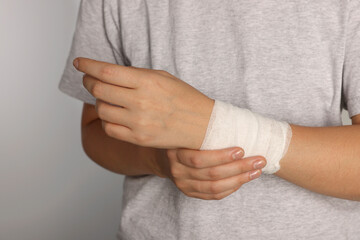 Woman with wrist wrapped in medical bandage on light grey background, closeup