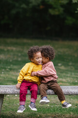 Black and Asian twins hugging and smiling at park 