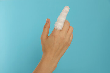 Woman with finger wrapped in medical bandage on on light blue background, closeup