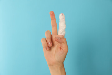 Woman with finger wrapped in medical bandage showing peace gesture on light blue background, closeup