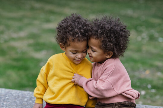 Black twins hugging on bench in park 