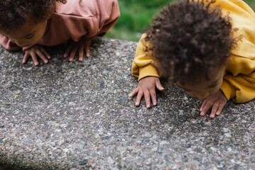 Two mixed race toddlers leaning over cement bench