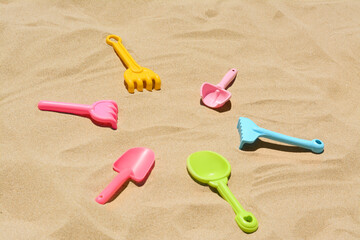 Bright plastic rakes and shovels on sand. Beach toys