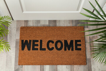 Door mat with word Welcome on wooden floor in hall, top view