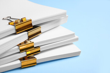 Many sheets of paper with golden clips on light blue background, closeup