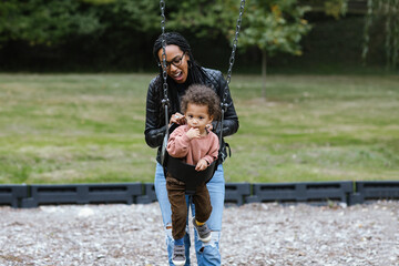 Black mother pushing mixed race child on swing at park - Powered by Adobe