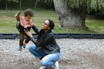 Mother playing with toddler on swing at park