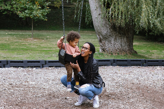 Mom Pushing Toddler On The Swing At Park