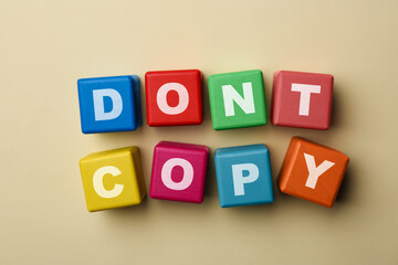 Colorful cubes with words Don't Copy on beige background, flat lay. Plagiarism concept