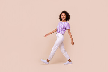 Fototapeta na wymiar Full length photo of funny pretty lady wear violet t-shirt walking empty space isolated beige color background