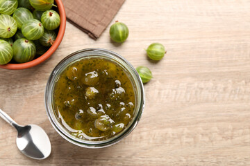 Jar of delicious gooseberry jam and fresh berries on wooden table, flat lay. Space for text