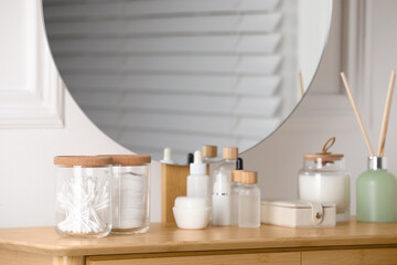 Glass jars with cotton swabs and pads near cosmetic products on dressing table