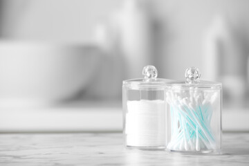 Plastic jars with cotton pads and swabs on white countertop in bathroom. Space for text
