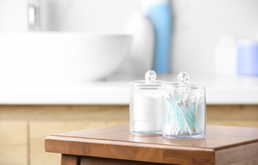 Fototapeta na wymiar Plastic jars with cotton pads and swabs on wooden stool in bathroom. Space for text
