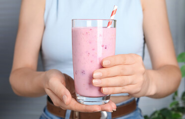 Woman holding glass of tasty raspberry smoothie indoors, closeup