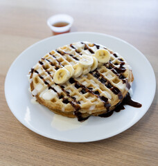 Delicious morning waffle plate from a restaurant with sweet banana, chocolate and syrup on waffles. Sugar Breakfast food on morning.