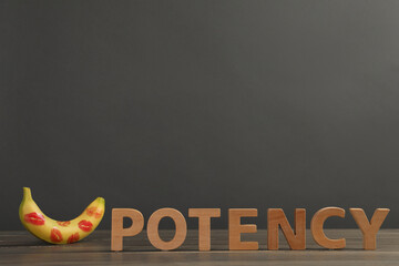 Word Potency made of letters and banana with red lipstick marks on wooden table against grey...