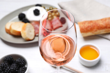 Glass of delicious rose wine and snacks on white table, closeup