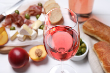 Glass of delicious rose wine and snacks on white table, closeup