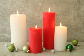 Burning candles with Christmas baubles on light grey table