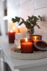 Burning candles on mantel near white wall indoors