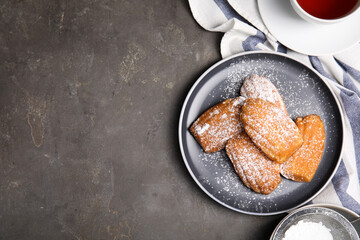 Delicious madeleine cakes with powdered sugar and tea on grey table, flat lay. Space for text