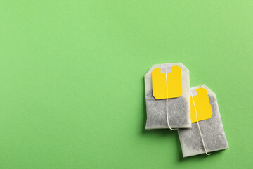 New tea bags with tabs on green background, flat lay. Space for text