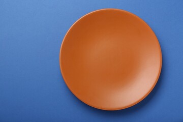 Empty orange ceramic plate on blue background, top view. Space for text