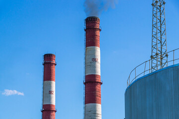 Black smoke comes out of the production high pipe. Industrial zone of the factory territory. Pipes in the factory and a large steel tank with fuel. Production technologies at the enterprise.
