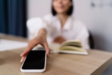 Faceless woman picking up smartphone in office