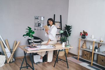 Cheerful self employed woman with book working in modern workspace