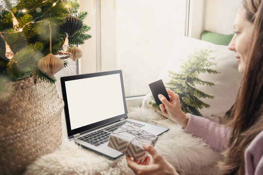 Christmas sales. Woman orders Christmas gifts online using a bank card with laptop in home interior. Xmas concept. Planning holidays.